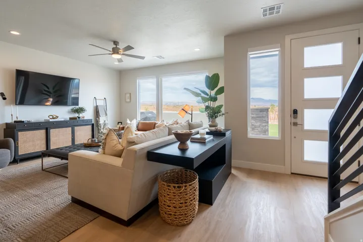 Open-concept living area featuring light wood-finish flooring, a contemporary ceiling fan, and large windows with distant mountain scenery