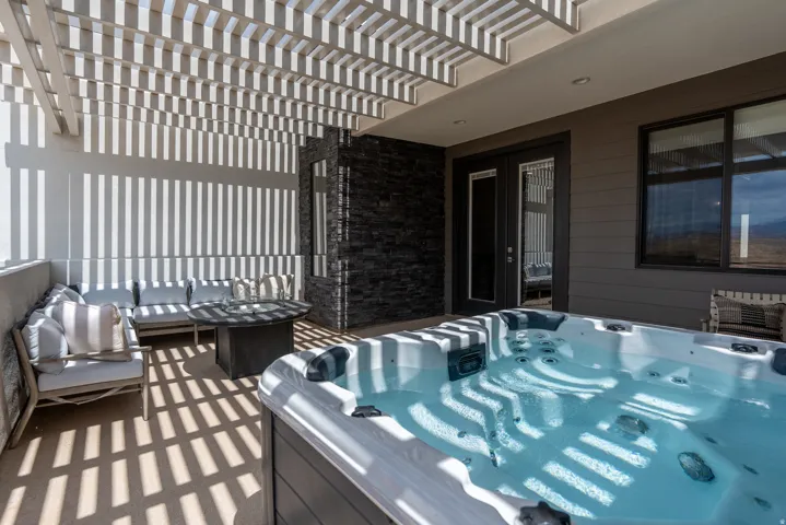 Outdoor patio featuring a built-in spa, slatted pergola, and dark stacked stone accent wall