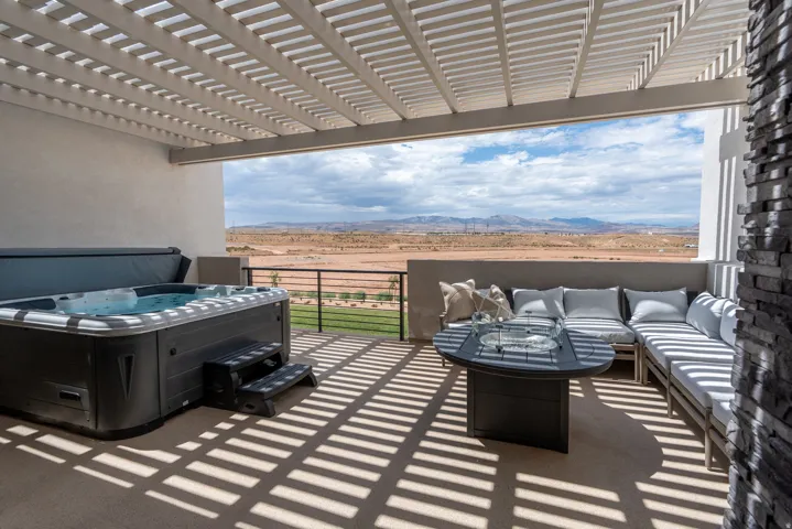 Covered outdoor patio featuring a slatted pergola, built-in spa, stone accent column, and expansive desert landscape