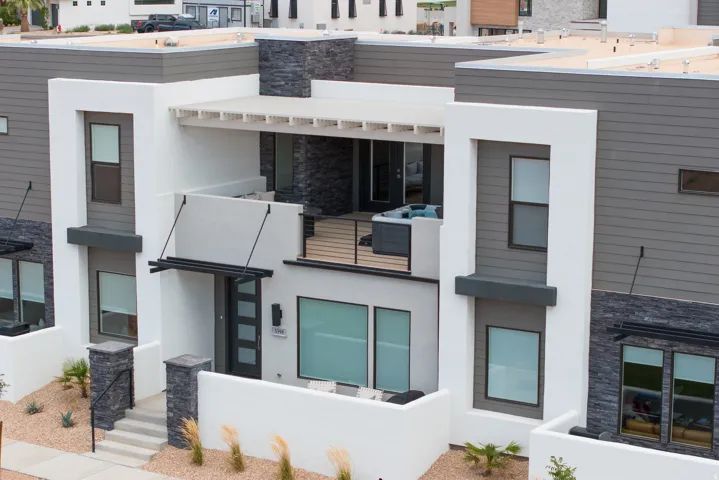 Contemporary multi-story exterior featuring a private balcony with a built-in spa, a ground-level patio, stacked stone accents, horizontal siding, and a modern entry door with sidelights