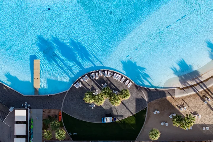Expansive water feature with a pier, surrounded by a paved patio area, sand beach, and green spaces