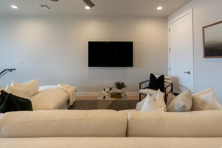 Spacious living area featuring light gray walls, recessed lighting, wood-finish flooring, a contemporary ceiling fan, and a white interior door with a brushed nickel lever handle