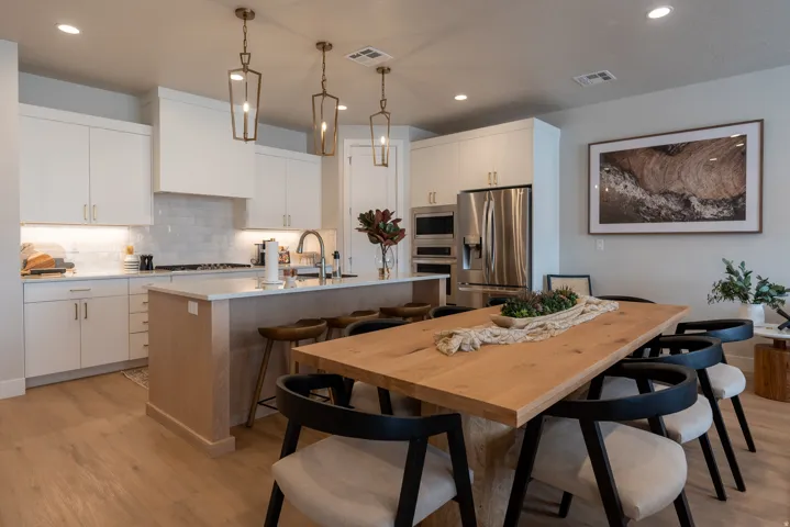 Bright kitchen featuring white cabinetry, stainless steel appliances, a center island with bar seating, wood-finish flooring, and pendant lighting