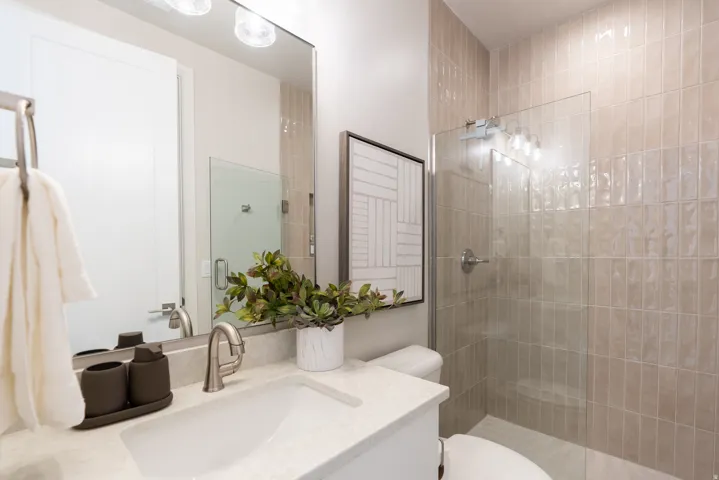Bathroom featuring a frameless glass shower enclosure, full wall tile surround, white vanity with integrated sink, stone-finish countertop, and brushed nickel fixtures