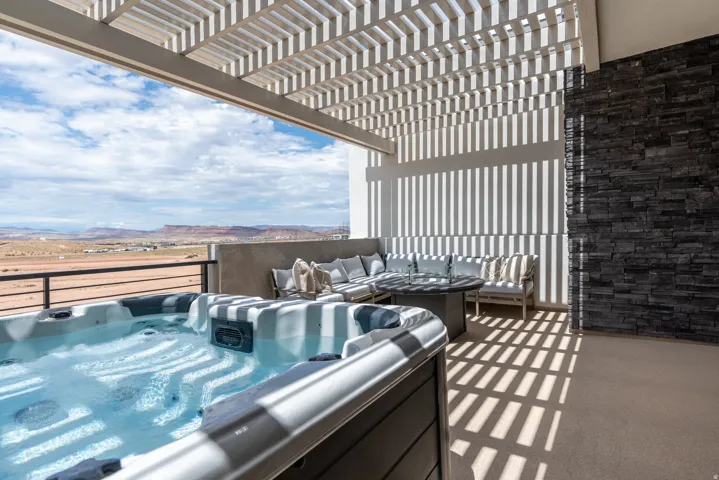 Outdoor patio featuring a built-in spa, a slatted pergola overhead, and a stacked stone accent wall