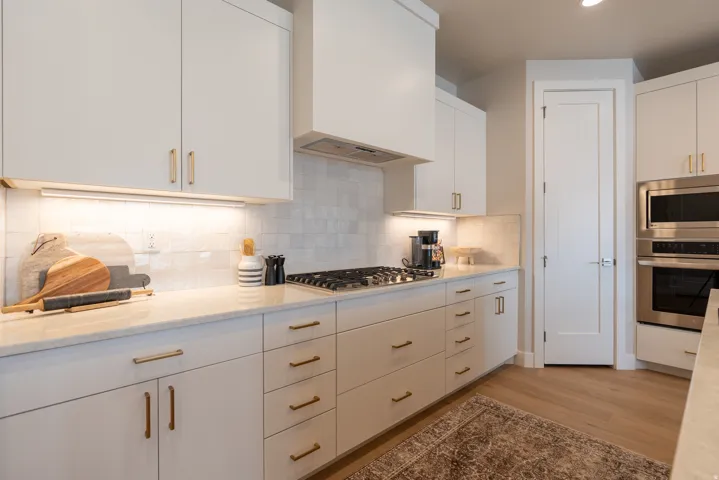 Modern kitchen featuring white cabinetry with brass hardware, a gas cooktop, light-colored countertops, a tile backsplash, and stainless steel built-in appliances including a microwave and oven