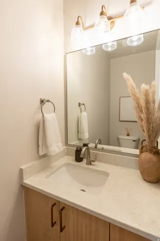 Vanity featuring a light wood-finish cabinet with bronze hardware, a solid surface countertop with an integrated sink, and a brushed nickel faucet