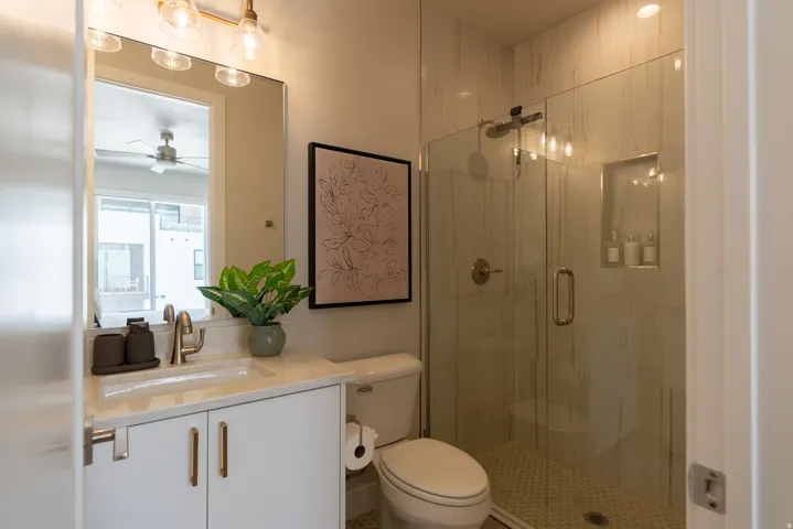 Bathroom featuring a glass-enclosed shower with tile surround, a built-in shower niche, a hexagonal tile shower floor, a vanity with an integrated sink and light-toned countertop, and a vanity light fixture