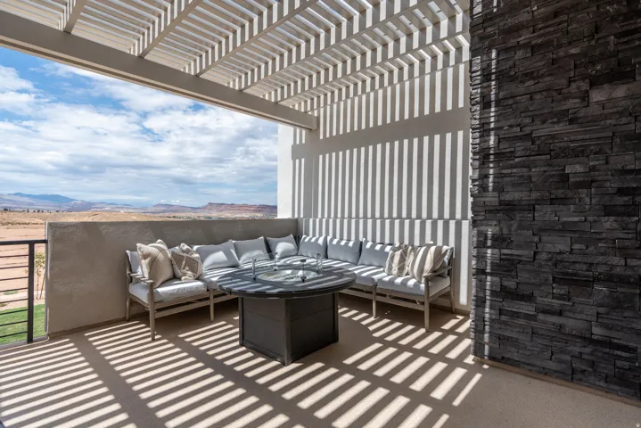 Covered outdoor patio featuring a slatted pergola, stacked stone wall, stucco exterior, and a built-in fire pit table