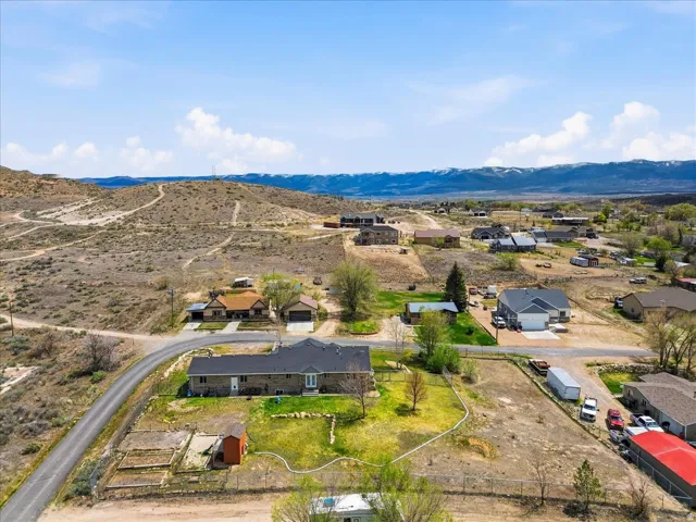 Aerial perspective showcasing multiple properties within a rural landscape, featuring a paved road and mountainous backdrop