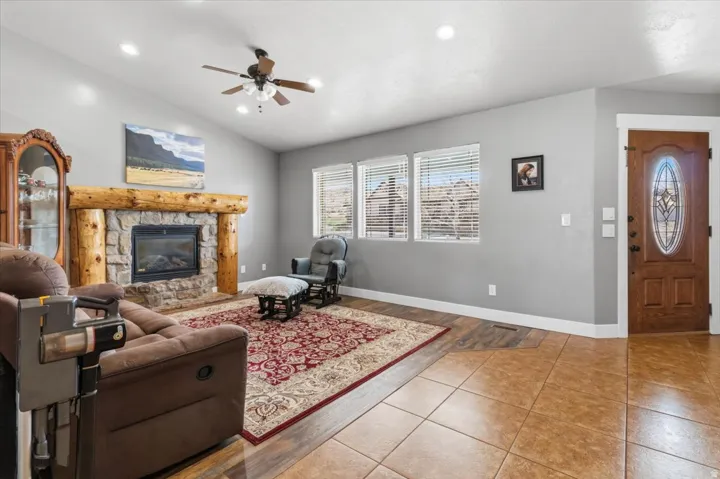 Living space featuring a stone-clad fireplace with a log mantel, vaulted ceiling with recessed lighting and a ceiling fan, and multiple windows