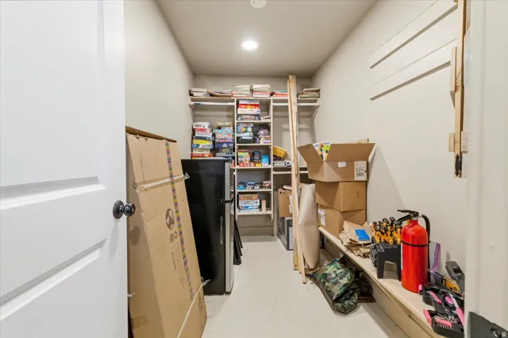 Storage room featuring built-in shelving, painted walls, overhead recessed lighting, a white door with a dark doorknob, and light-colored flooring