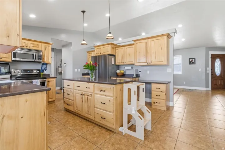 Kitchen featuring light wood cabinetry, dark countertops, a central island, stainless steel appliances, and tiled flooring