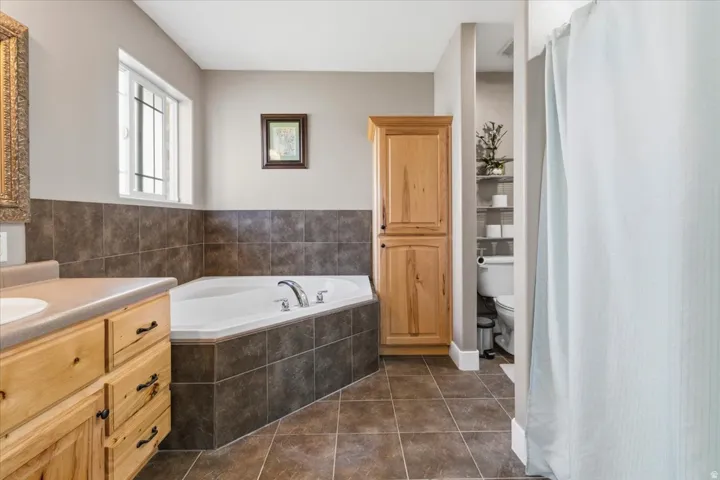 Bathroom featuring a built-in corner soaking tub with tile surround, wood-finish vanity with countertop and integrated sink, and floor-to-ceiling wood-finish cabinetry