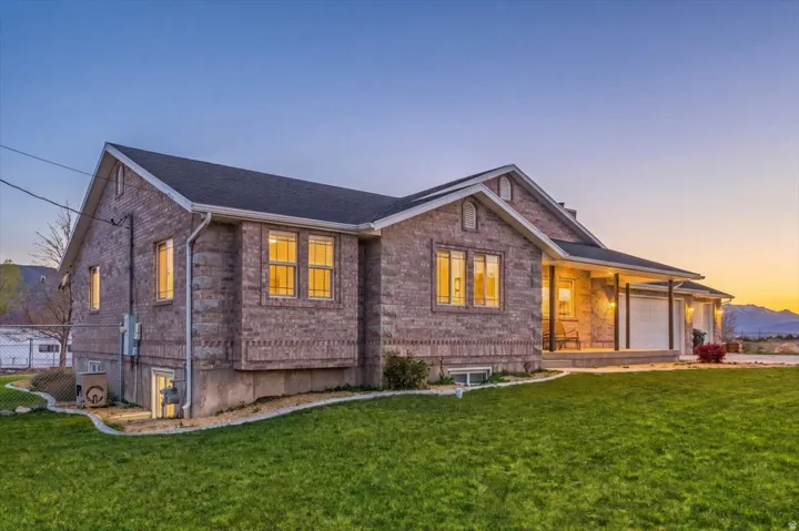 Brick exterior with a covered porch, attached garage, and a lush green lawn