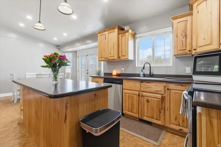 Kitchen featuring wood cabinetry, dark countertops, a stainless steel dishwasher, an undermount sink with a black gooseneck faucet, and recessed lighting