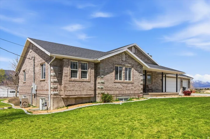Brick exterior residence featuring a covered front porch, dual garage doors, a dark shingle roof, multiple windows, and a grassy front yard