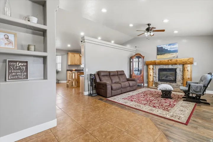 Living area featuring a stone fireplace with a log mantel, vaulted ceiling, recessed lighting, and a ceiling fan