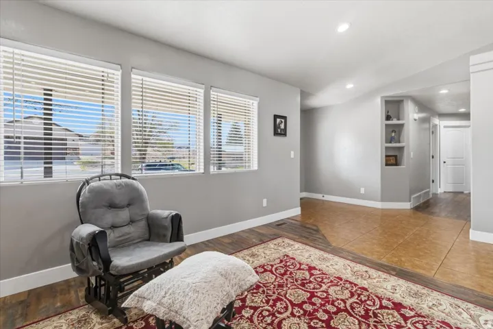 Living area featuring three large windows with horizontal blinds, recessed lighting, built-in display shelving, wood-finish flooring, and earth-toned tile flooring