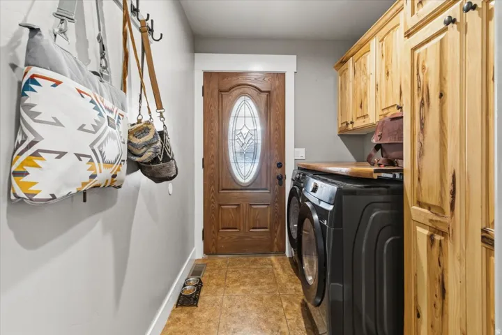 Laundry area featuring a wood-finish door with an oval glass insert, tile flooring, built-in cabinetry, and a wood countertop above front-loading appliances