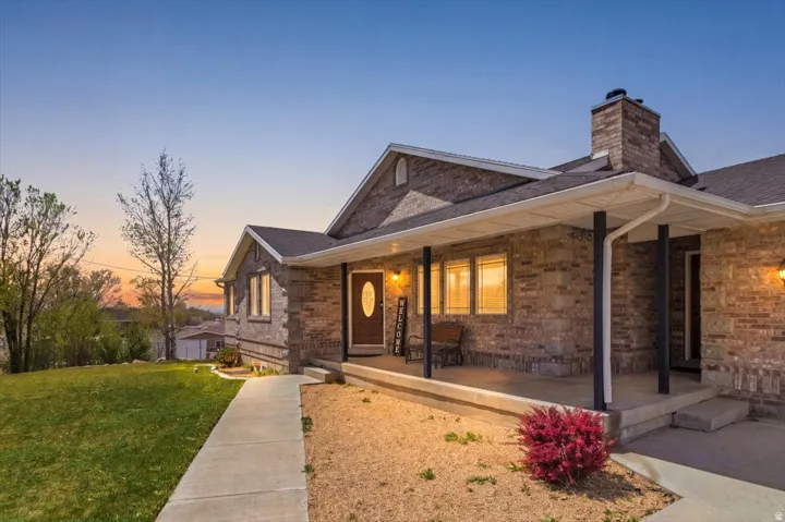 Brick and stone facade residence featuring a covered front porch, a prominent brick chimney, gabled rooflines, and a concrete walkway
