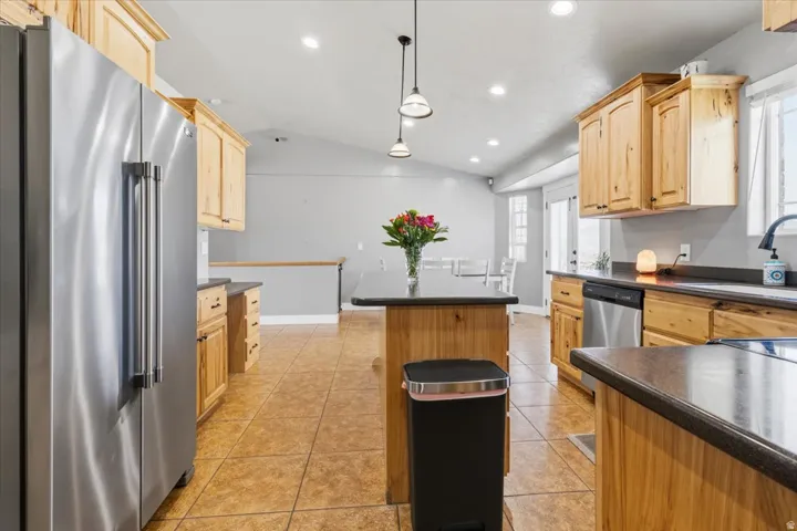 Spacious kitchen featuring light wood cabinetry, dark countertops, a central island, stainless steel appliances, and tile flooring