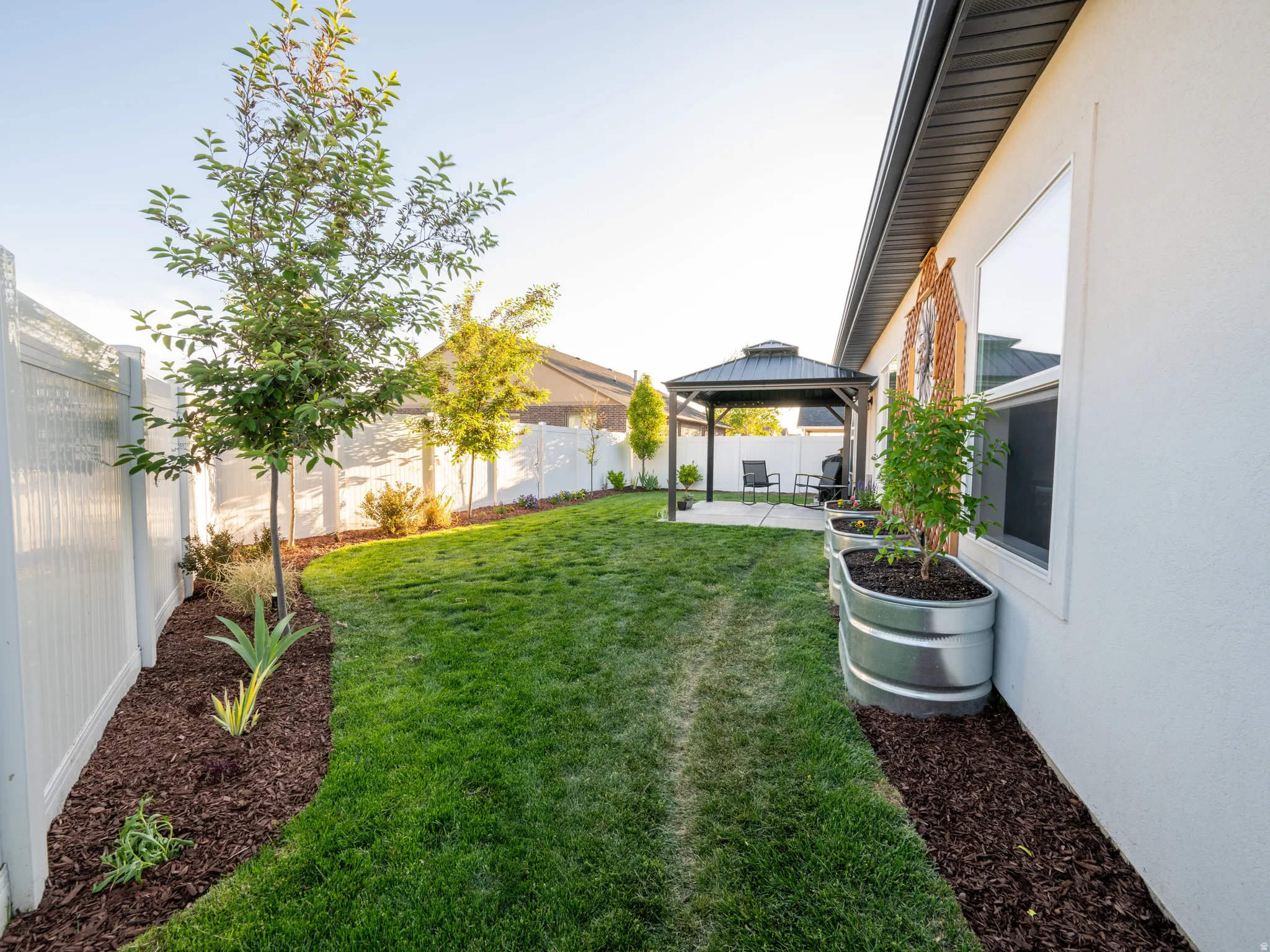 Spacious backyard featuring a manicured lawn, established trees, and a white vinyl privacy fence