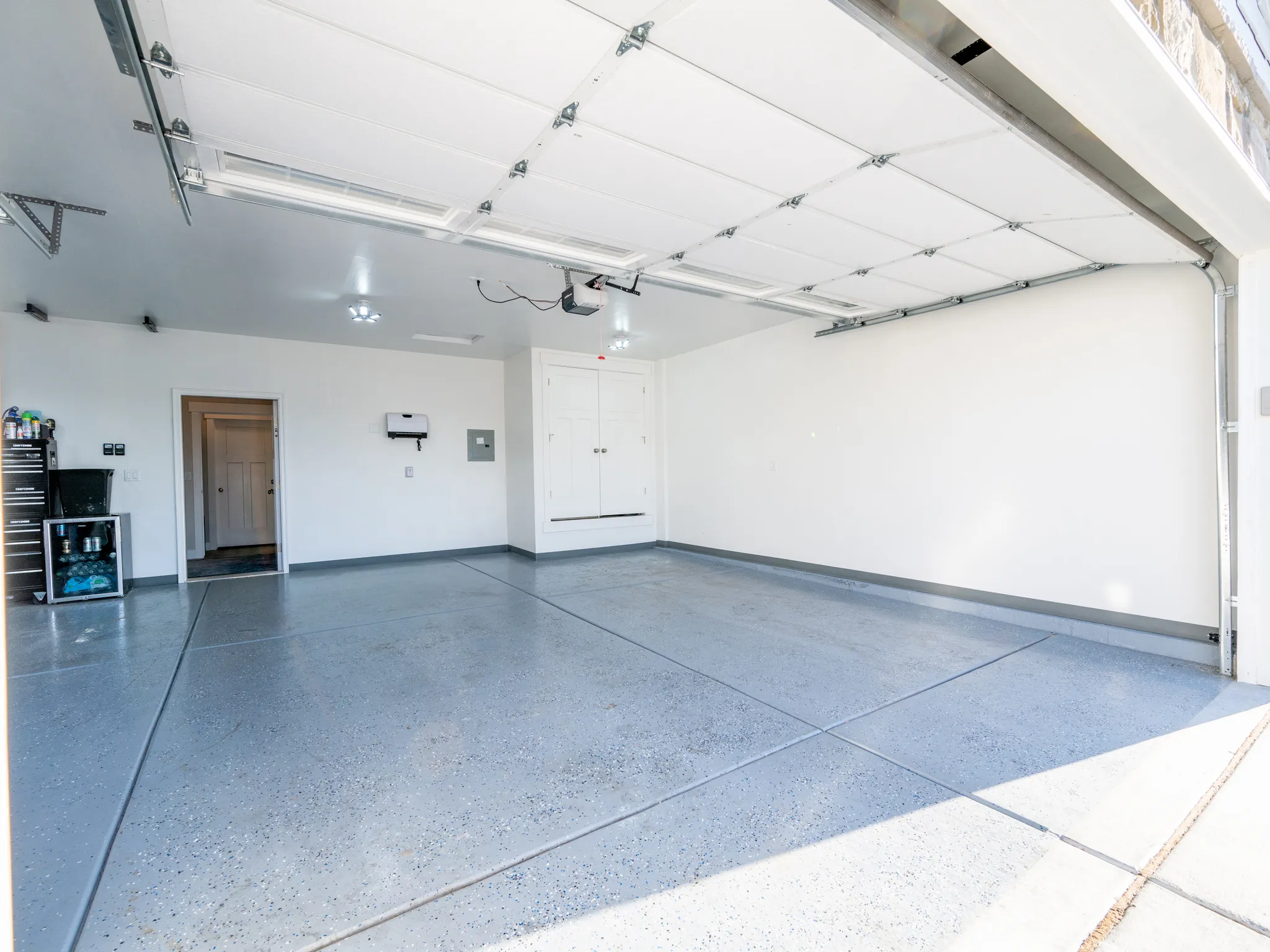Spacious garage featuring a durable epoxy-coated floor, integrated ceiling lighting, white overhead garage door, built-in storage cabinetry, and a service door