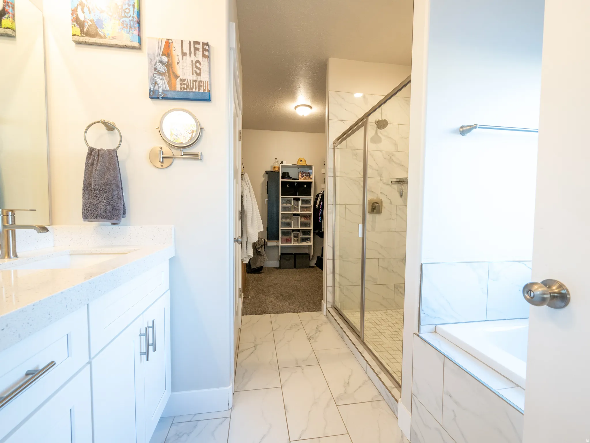 Bathroom featuring a white vanity with a quartz-finish countertop, brushed nickel faucet, large walk-in shower with glass enclosure, white rectangular bathtub, and white tile flooring