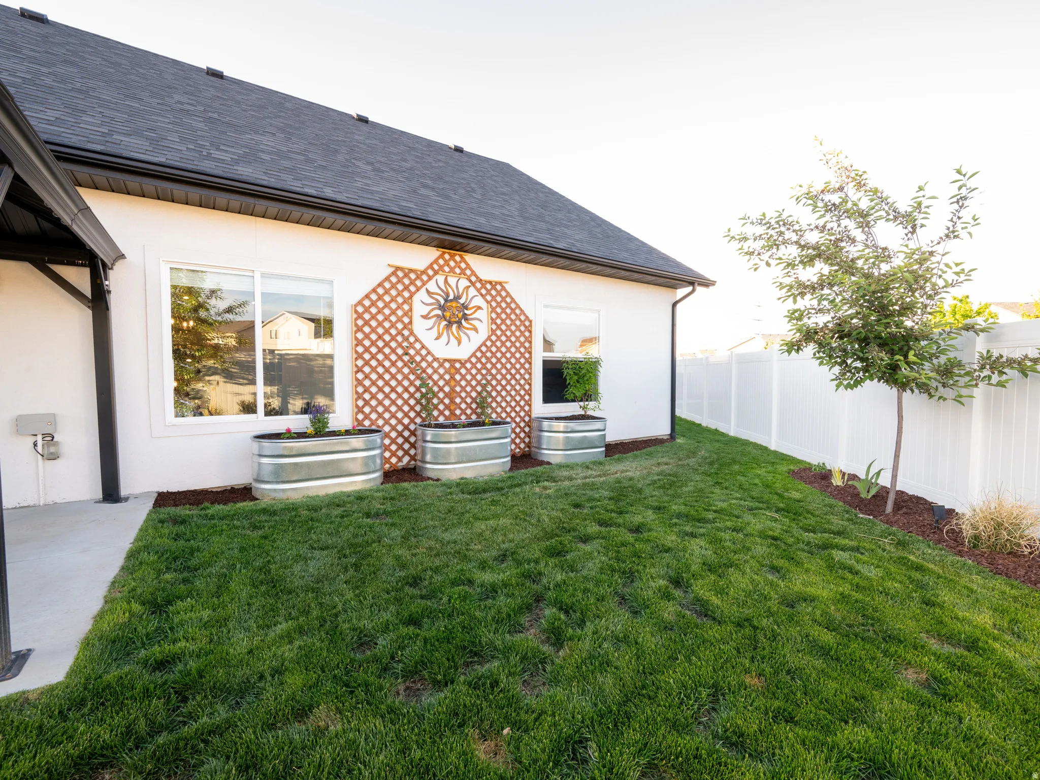 Expansive rear yard featuring a white privacy fence, mature trees, and a manicured lawn
