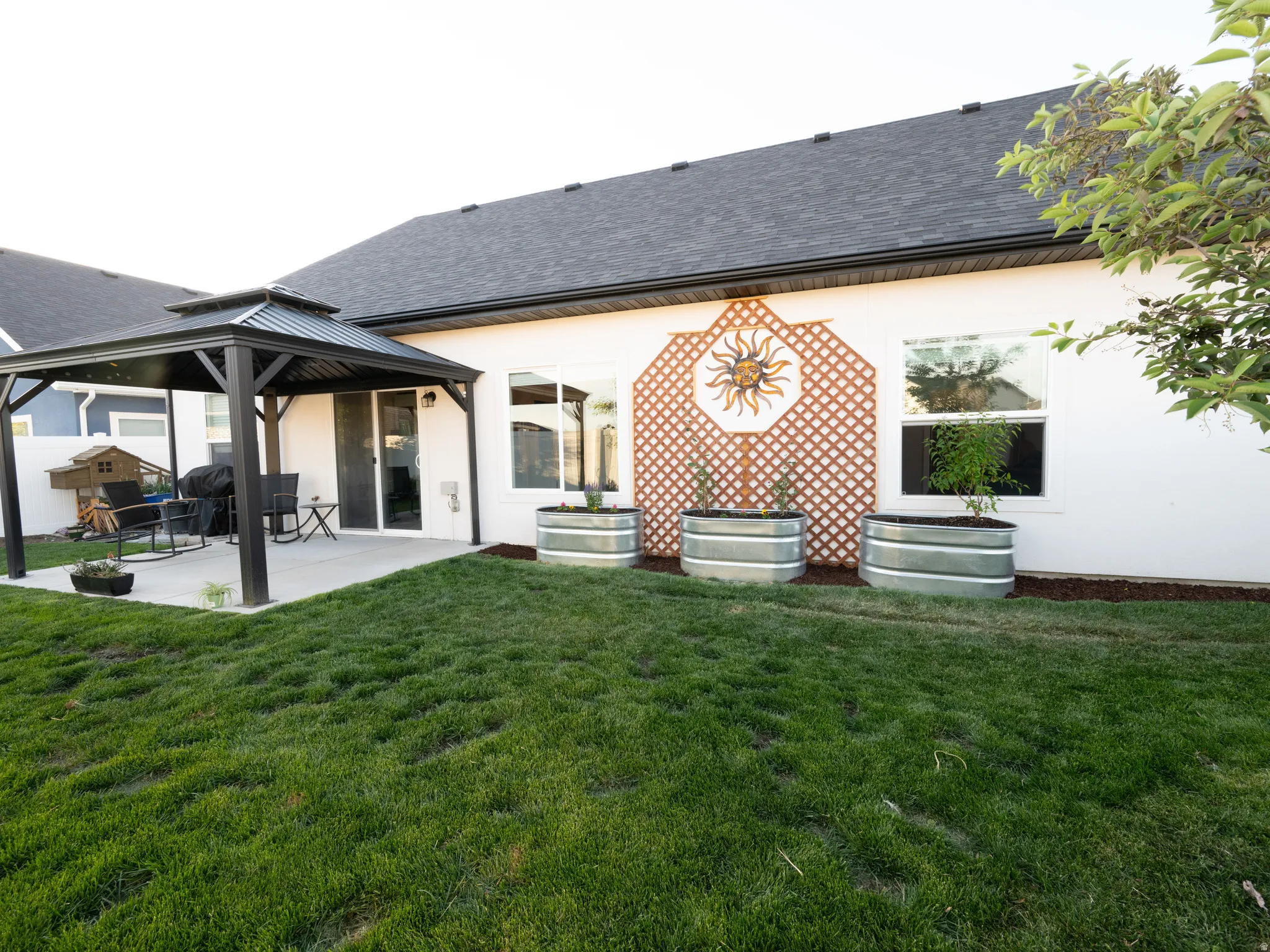 Expansive backyard featuring a concrete patio, covered gazebo with a tiered roof, and a sliding glass door entry