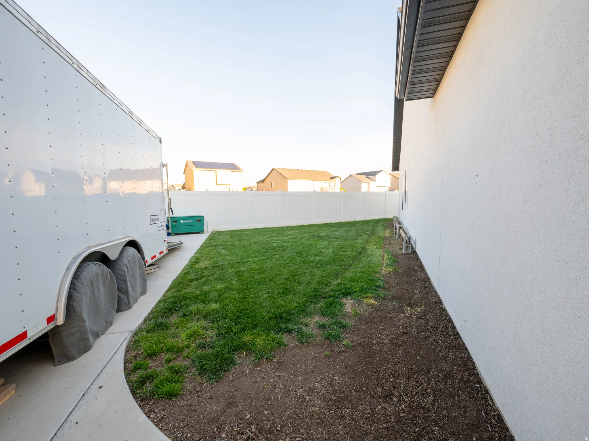 Expansive side yard featuring a curved concrete path, a newly seeded lawn area, and a white privacy fence