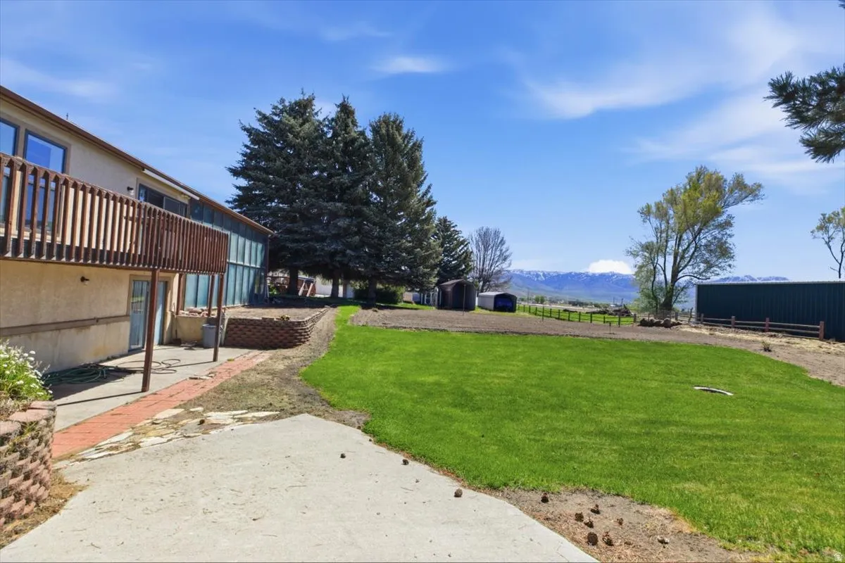 Expansive green lawn with mountain scenery, featuring a multi-level deck, a concrete patio, and a brick-lined walkway