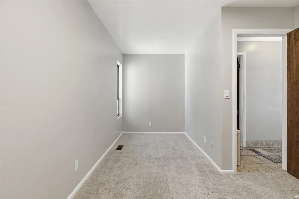 Light gray wall paint with white trim, new gray carpet, a window, and a recessed floor vent