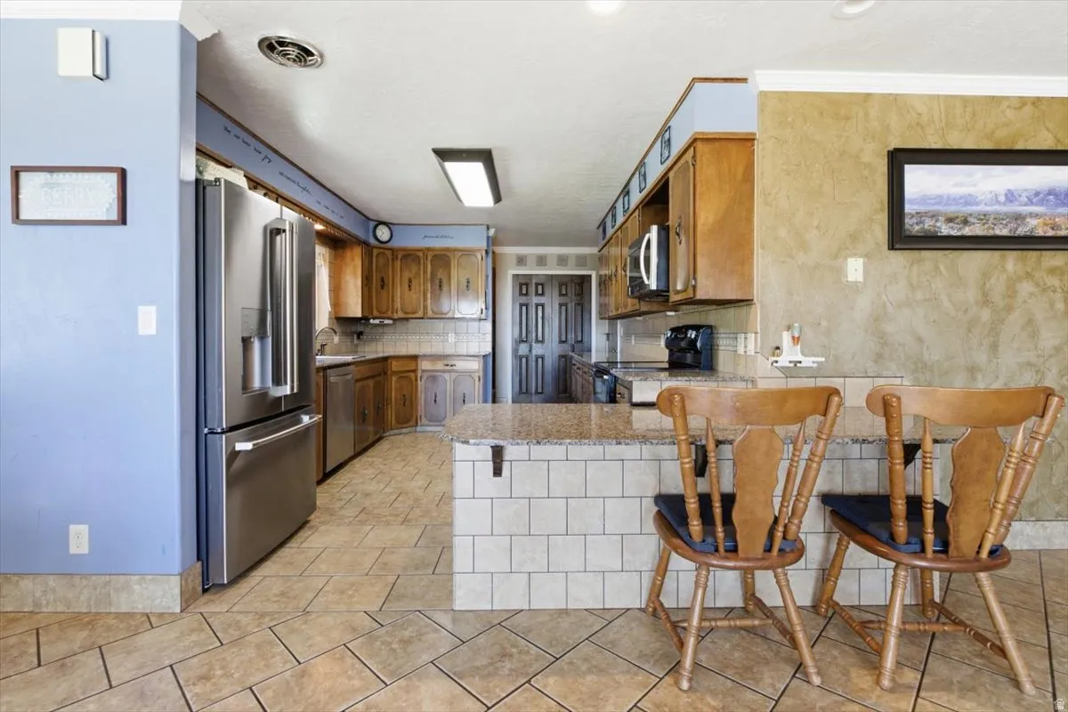 Kitchen featuring tile flooring, stainless steel refrigerator, wood cabinetry, stone countertops, and a tiled breakfast bar