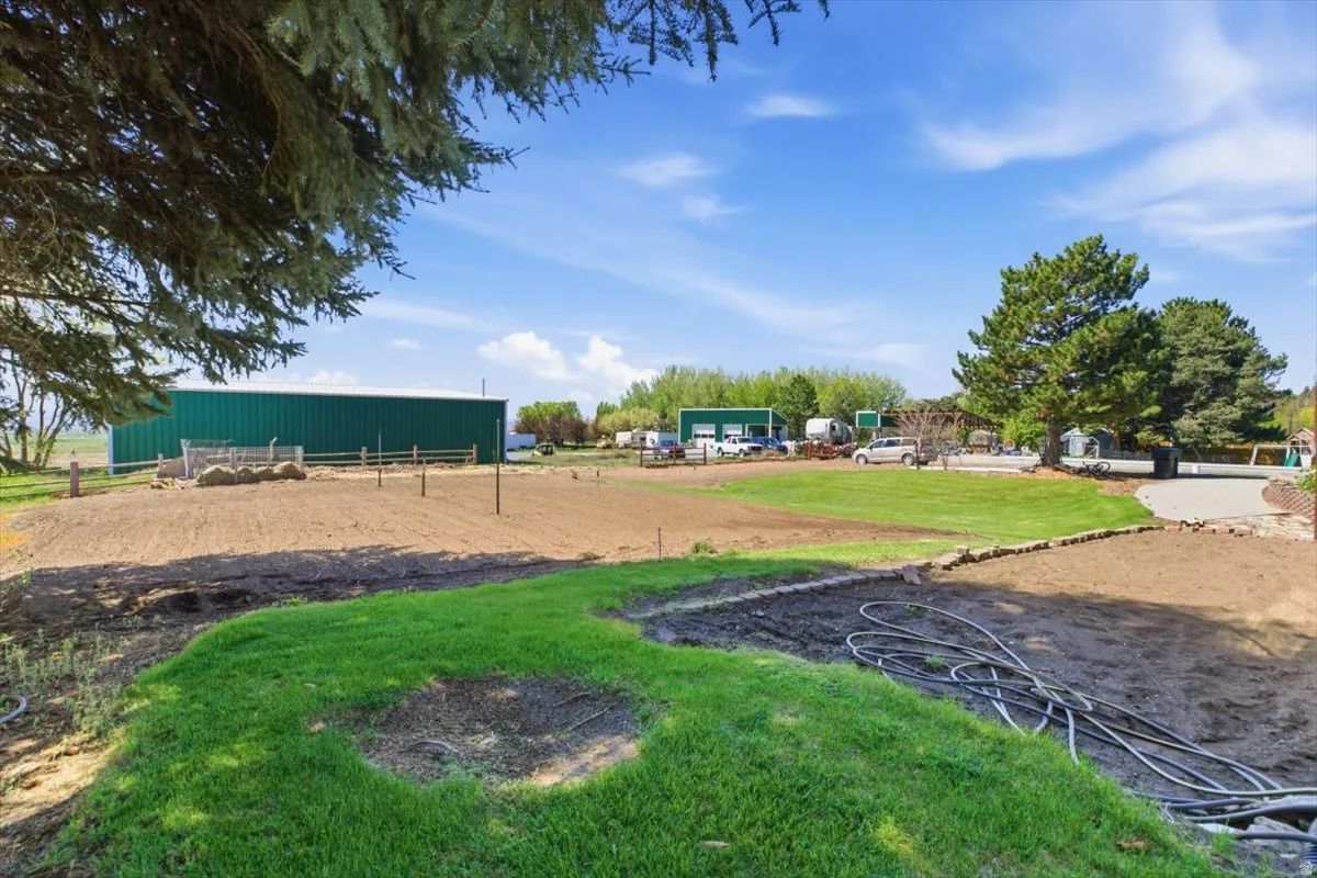 Expansive grounds featuring a large green metal building, a manicured lawn, mature trees, and a developed patio area