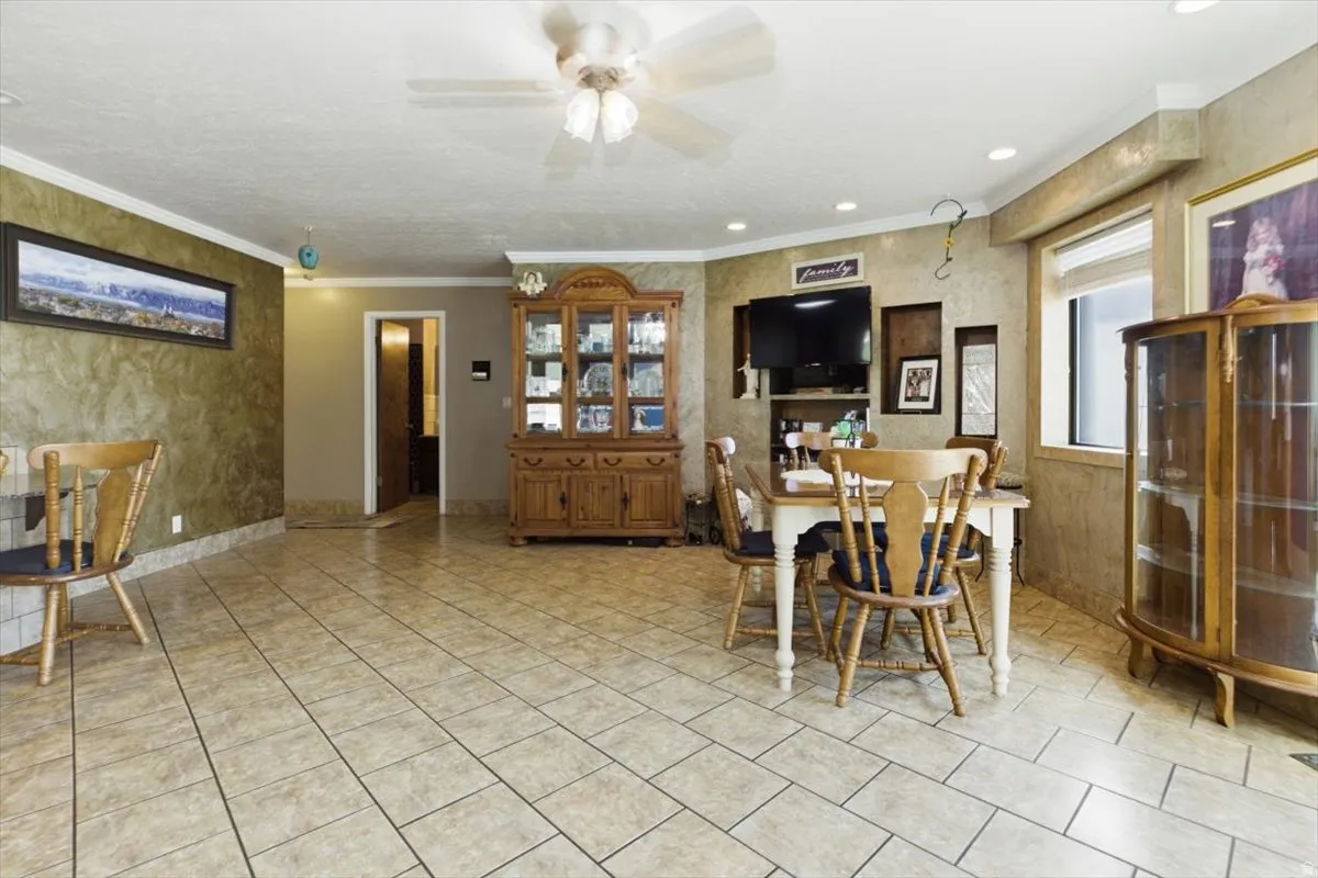 Spacious interior featuring tile flooring, crown molding, a ceiling fan, recessed lighting, and a large window