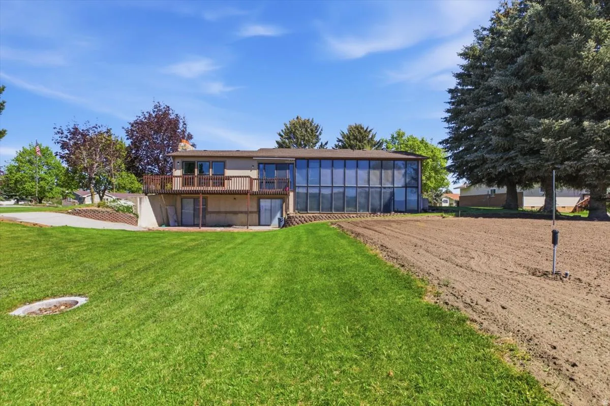Expansive backyard featuring a large sunroom with floor-to-ceiling windows, a wooden deck, and a lower-level patio with sliding glass doors