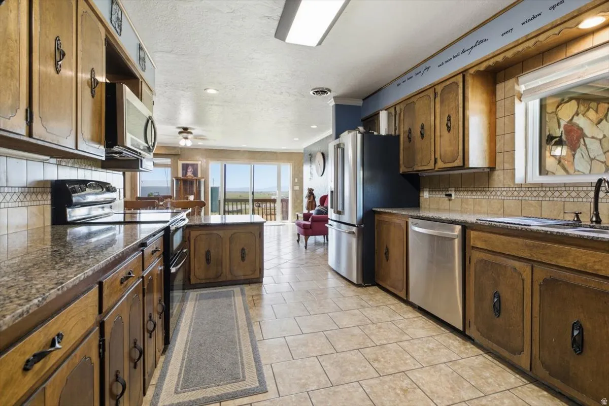 Kitchen featuring wood cabinetry, granite-finish countertops, stainless steel appliances, and tile flooring