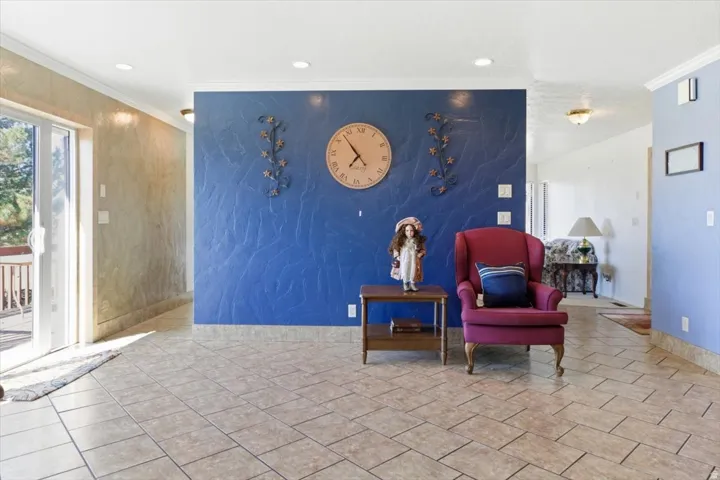 Spacious interior featuring tile flooring, textured accent walls, recessed lighting, crown molding, and a sliding glass door opening to an exterior deck