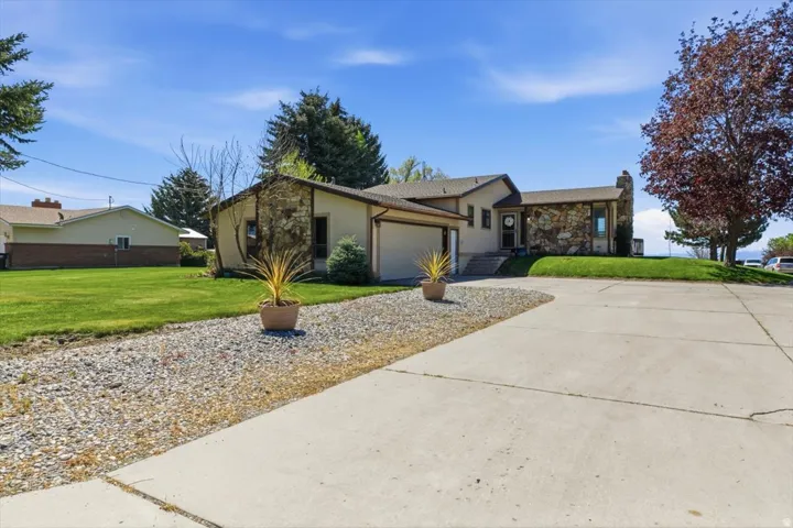 Exterior featuring a stone facade, beige stucco, a two-car garage, a concrete driveway, and a gravel pathway