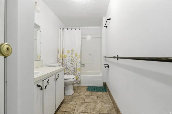 Full bathroom featuring a single vanity, a toilet, a tub with a shower, and tile flooring