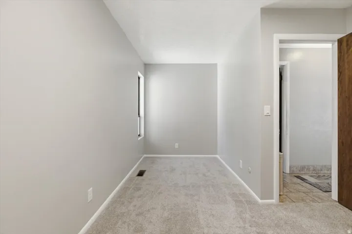 Light gray wall paint with white trim, new gray carpet, a window, and a recessed floor vent