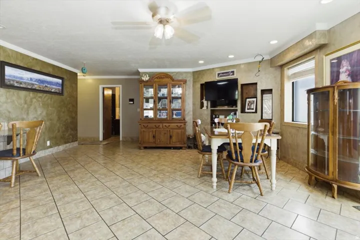 Spacious interior featuring tile flooring, crown molding, a ceiling fan, recessed lighting, and a large window