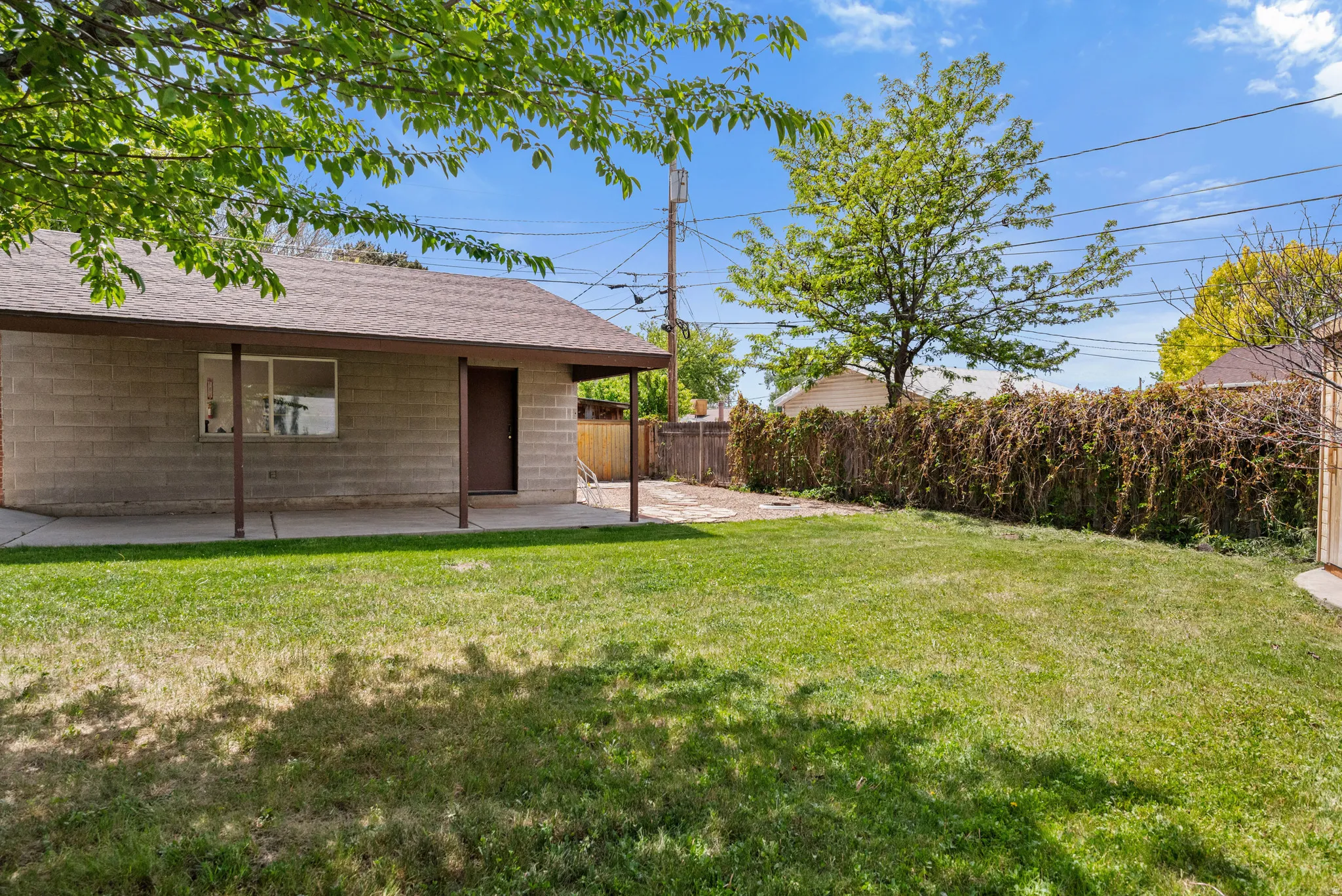 Generous backyard with a detached structure featuring a concrete block exterior, covered patio, and a shingled roof
