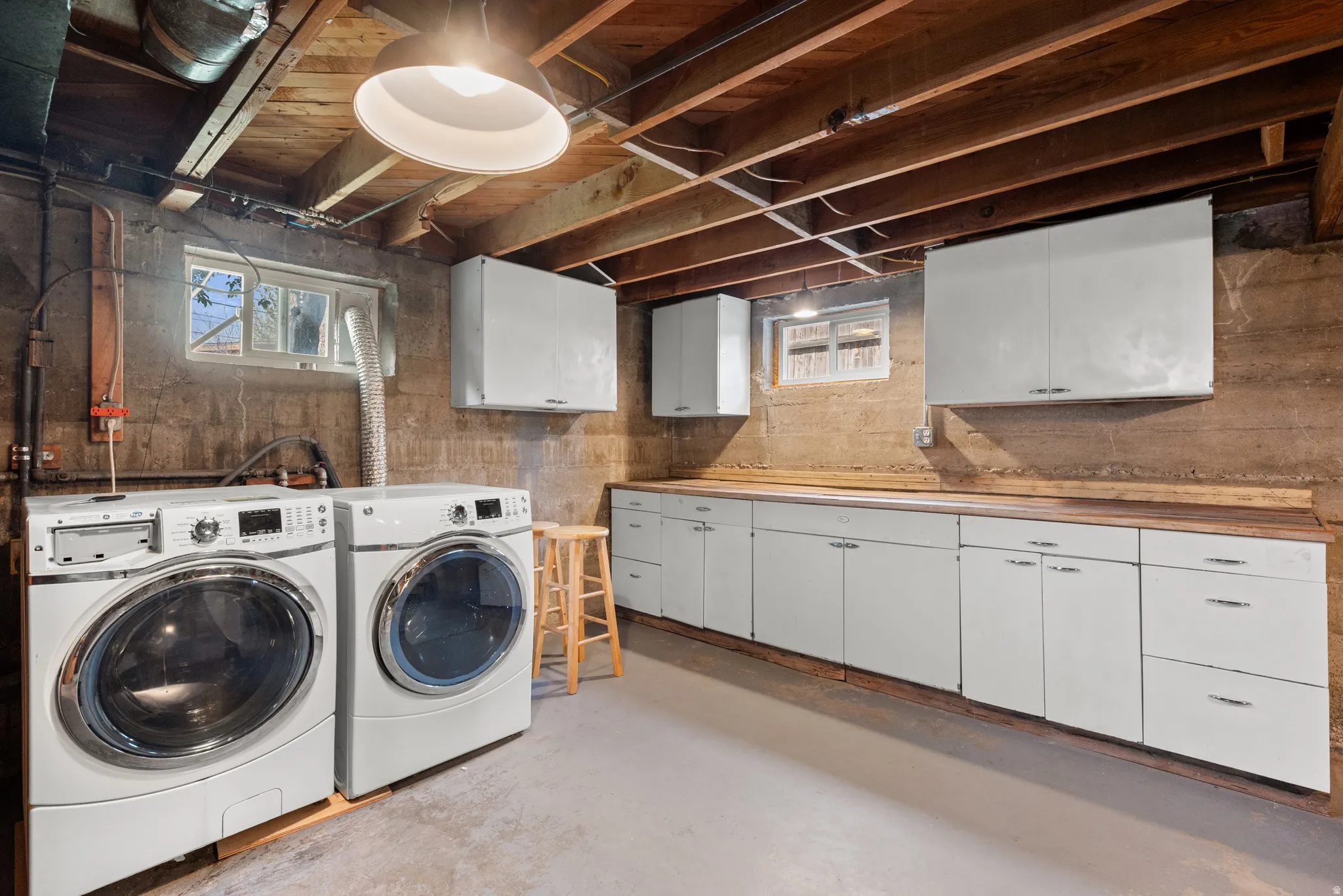 Dedicated laundry area featuring a washer and dryer, extensive white cabinetry, wood-finish countertops, exposed ceiling joists, and a concrete floor