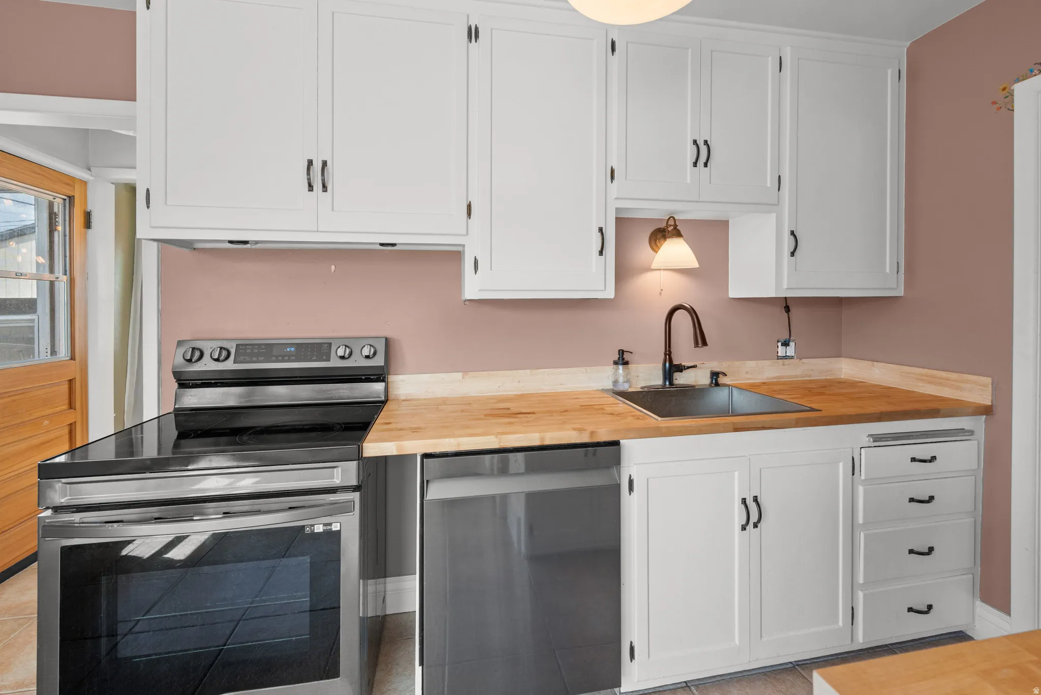 Kitchen featuring white shaker-style cabinetry with dark hardware, butcher block countertops, stainless steel appliances, and a dark basin sink with a gooseneck faucet