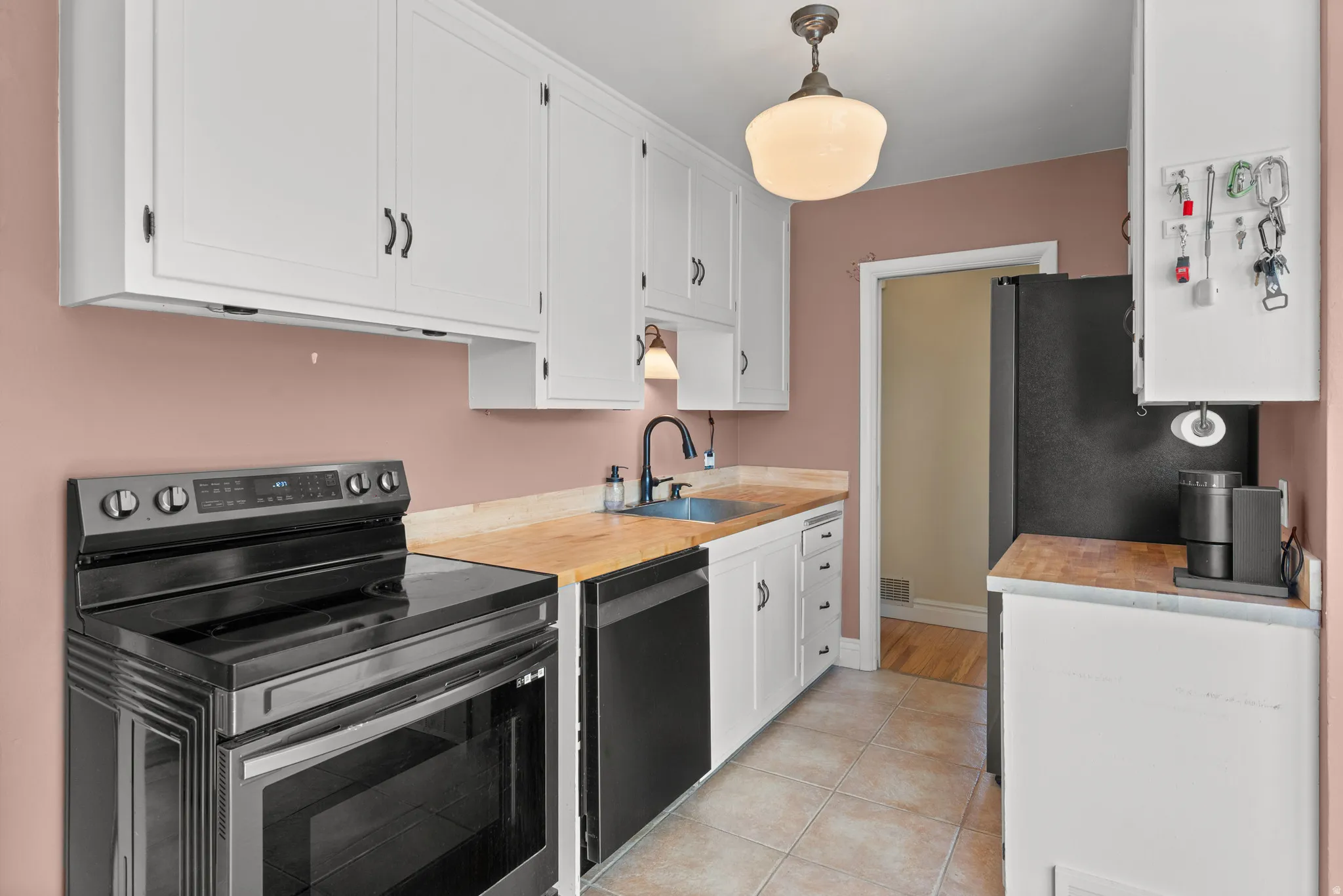 Kitchen featuring white cabinetry, light wood-finish countertops, and black appliances