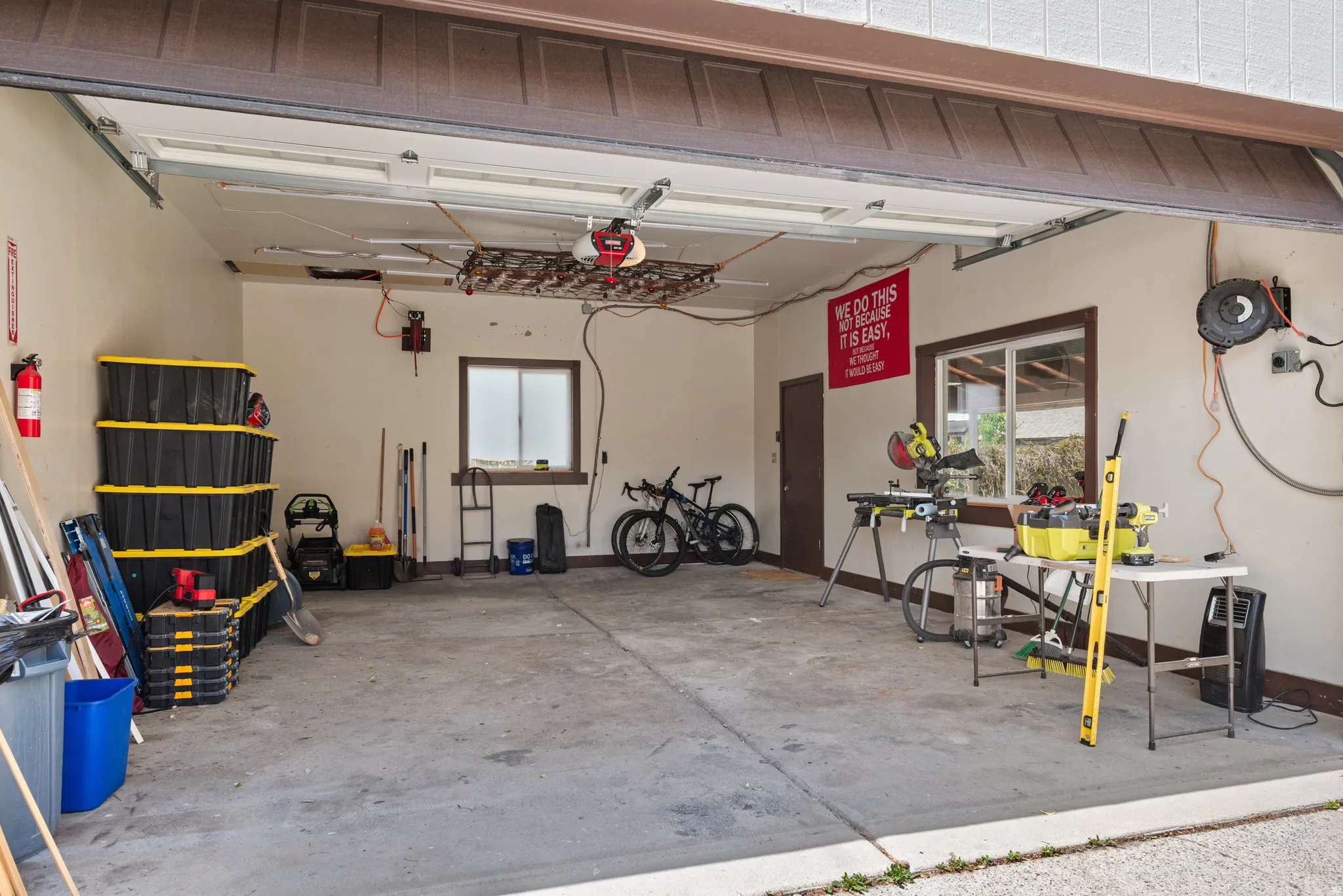 Spacious garage featuring a concrete floor, two windows with wood trim, a brown access door, and an overhead garage door mechanism