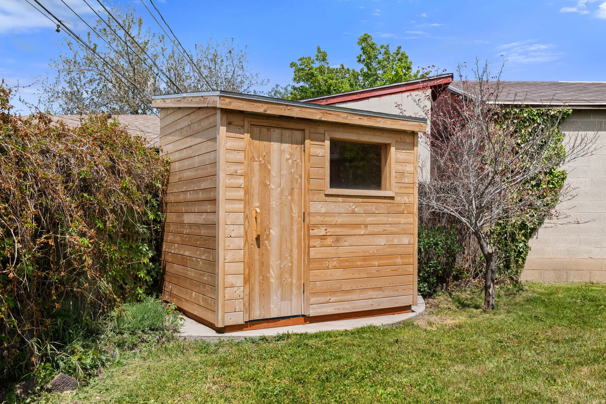 Wood-clad storage shed featuring a single window and a flat roofline, positioned on a concrete foundation